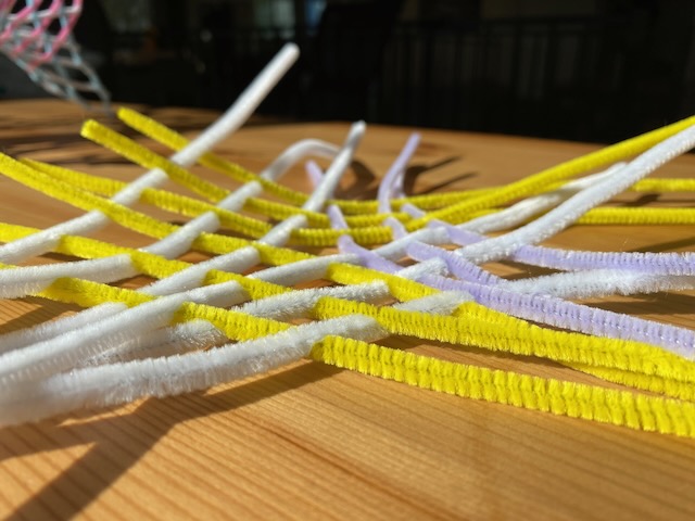  a square grid, woven out of pipe cleaners, with a pentagon in the center. Low angle picture, which bends slightly out of the plane